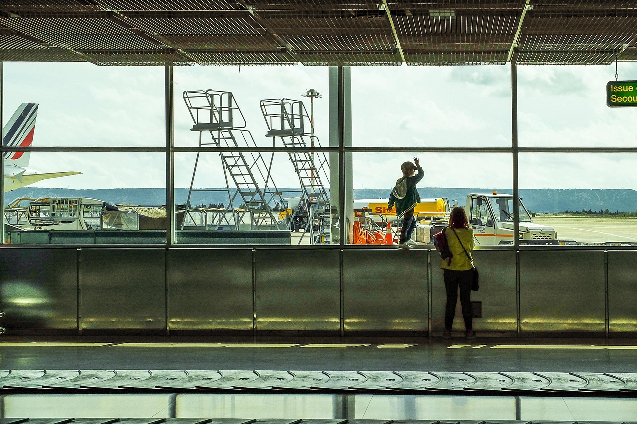 空港の窓から飛行機を眺める子ども。海外旅行で英語に触れるイメージ